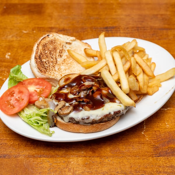 A cheeseburger topped with mushrooms, onions, and BBQ sauce, served with french fries and a side salad.