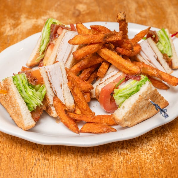 White plate with a turkey club sandwich and a pile of crispy sweet potato fries.