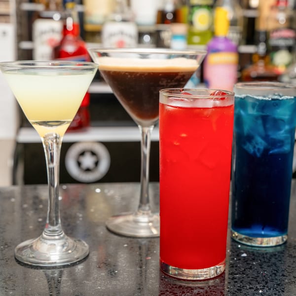 Four vibrant cocktails: yellow, espresso, red, and blue, on a speckled bar counter.