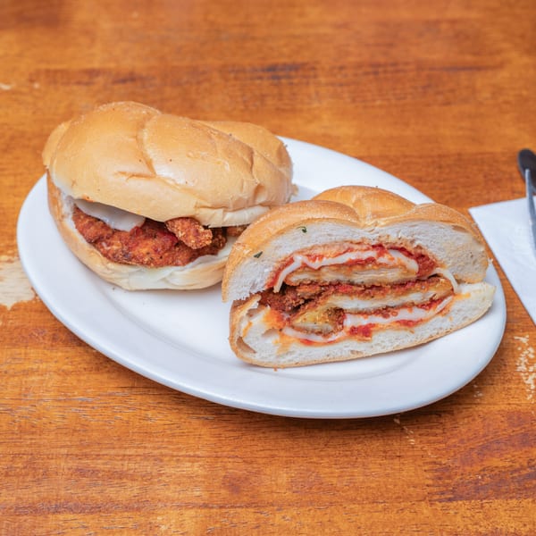One whole and one half chicken parmesan sandwich on a white plate.