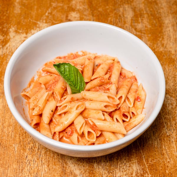 Penne pasta in creamy tomato sauce with a basil leaf in a white bowl.